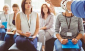 Hand of a trainer addressing group of females sitting in a conference hall. Female hand against defocused group of women attending seminar.