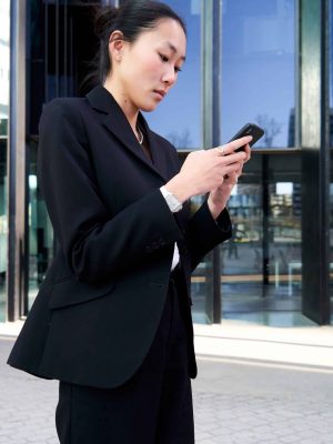 Vertical photo of young Asian businesswoman walking outside office building, using phone to work. Confident female CEO working on Financial Projects.